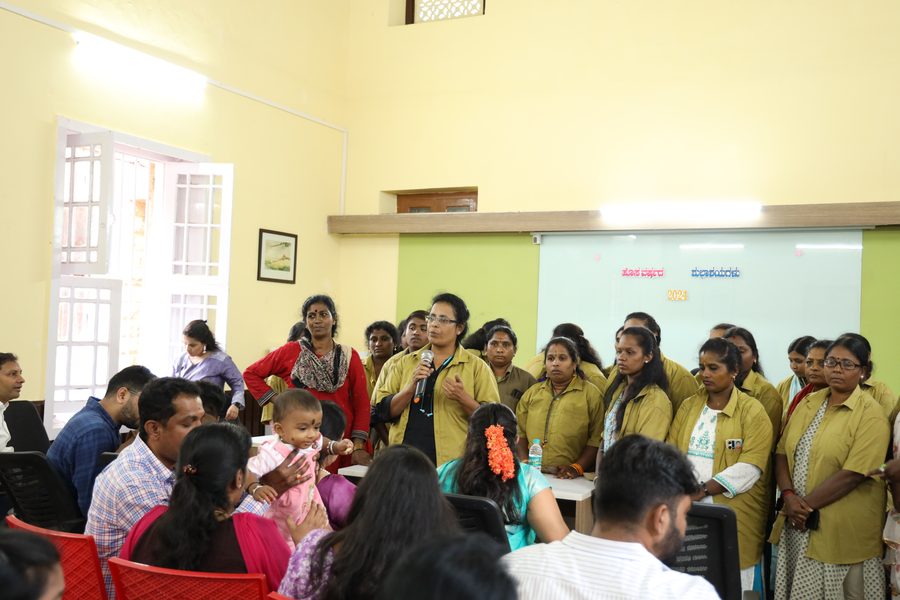 A Mahila Shakti driver speaking on a microphone at a community meeting