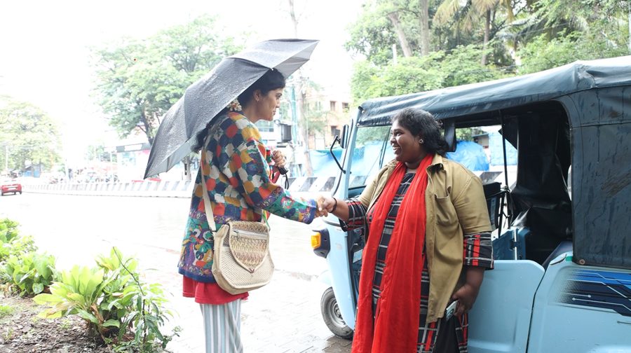 A Mahila Shakti driver greeting a passenger on a rainy Bengaluru street